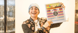 A smiling student holding the Teens in Print newspaper with their story featured on the cover