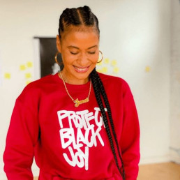 headshot of Jenee Osterheldt, smiling and looking down, wearing a red sweatshirt that says 