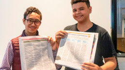 Two students standing side by side holding the Teens in Print newspaper open to their stories