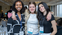 One staff member and two students smile with their arms around each other