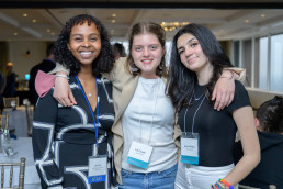 One staff member and two students smile with their arms around each other