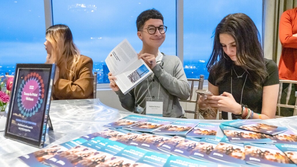 Smiling student holds up a booklet, held open to their piece of writing