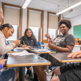 Adults sitting at desks in a circle, smiling and gesturing to each other