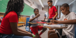 four students sit at mobile desks, working together on a group project