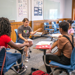 three students sit at mobile desks with educator in center
