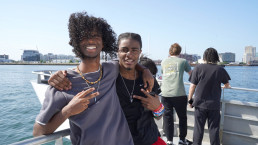 two students arm in arm, standing on the deck of a ferry in Boston Harbor
