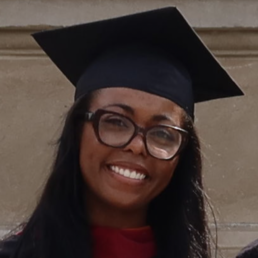 A woman with glasses and a graduation cap smiles.